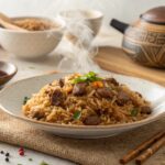 A plate of onion beef fried rice on a rustic wooden table with chopsticks beside it.