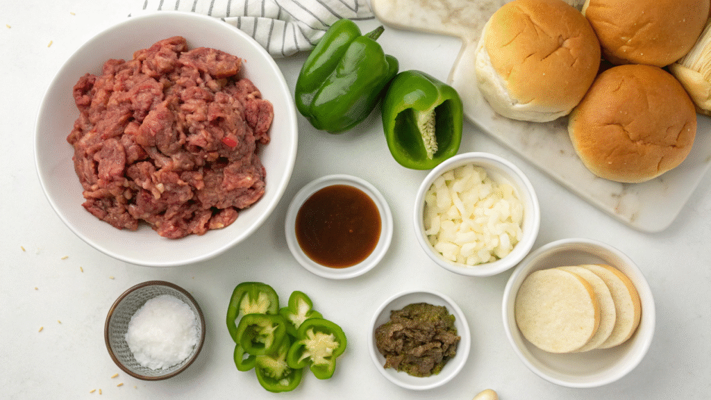 Flat lay of ingredients including beef, peppers, onions, cheese, buns, and seasonings.