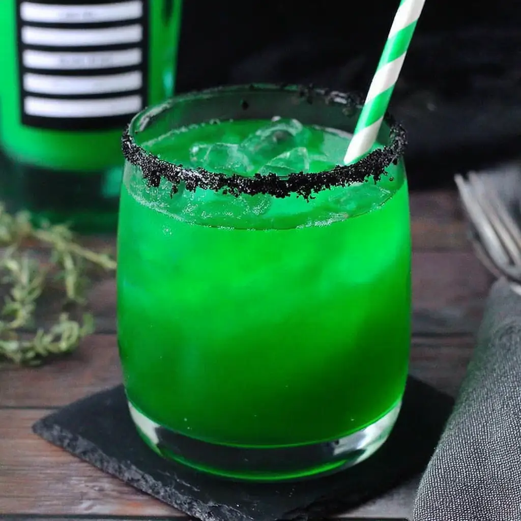 Beetlejuice Cocktail in a black-salt–rimmed glass with green glitter and gummy worm garnish