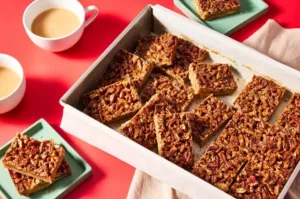 Delicious pecan pie bars topped with caramel and pecans on a white plate.