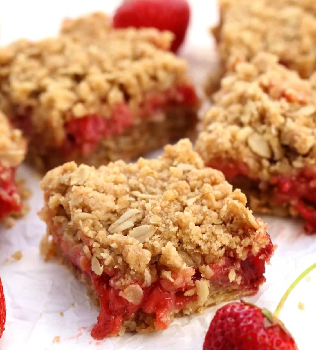 Vegan strawberry oat bars stacked on a plate, fresh strawberries beside them.