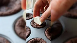 Hand placing a marshmallow half on a chocolate cookie cup in a mini muffin pan.